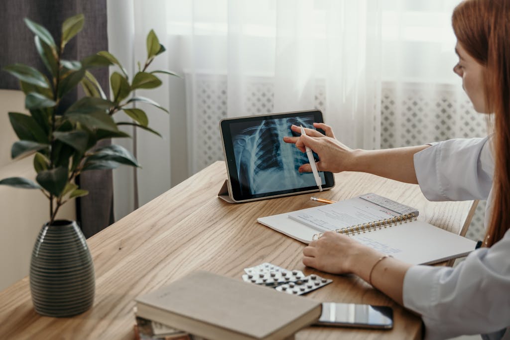 Healthcare professional examines X-ray image on tablet at desk with medical notes.